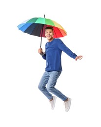 Young man with rainbow umbrella jumping on white background