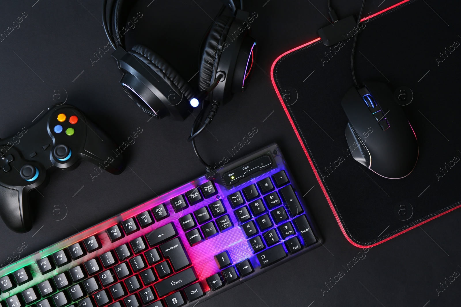 Photo of Computer mouse, RGB keyboard, game controller and headset on black background, flat lay