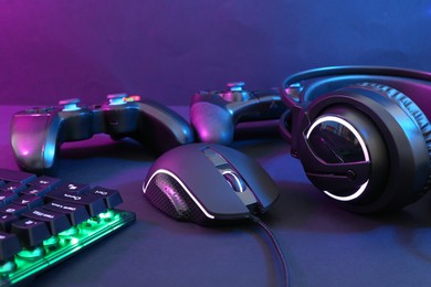 Computer mouse, headset, RGB keyboard and game controllers in neon lights on dark background, closeup