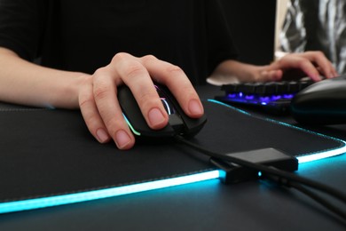 Gamer using modern wired computer mouse at dark table, closeup