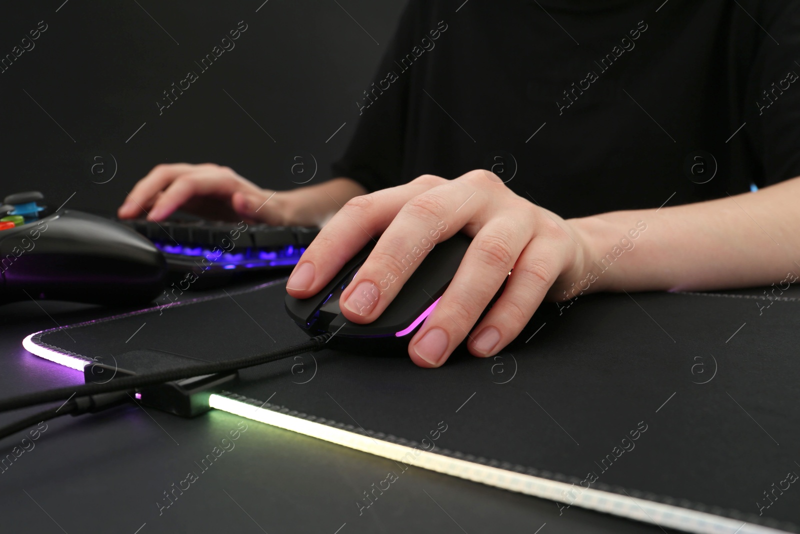 Photo of Gamer using modern wired computer mouse at dark table, closeup