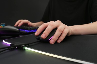 Photo of Gamer using modern wired computer mouse at dark table, closeup