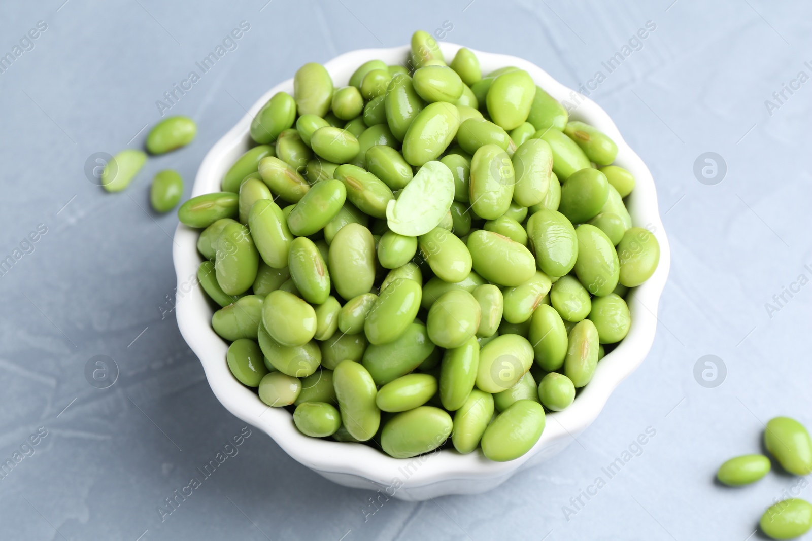 Photo of Fresh edamame soybeans in bowl on grey textured table, above view