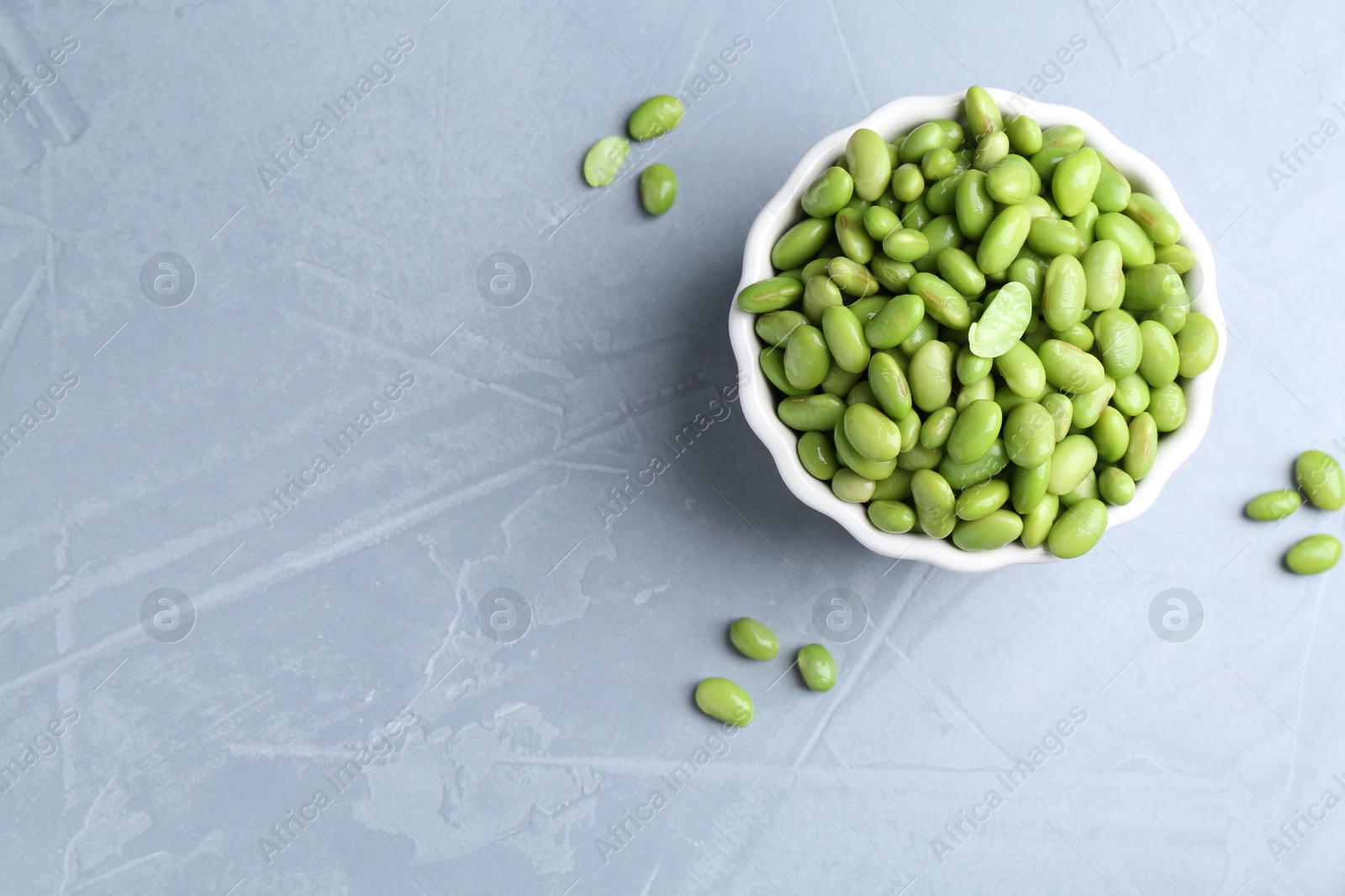 Photo of Fresh edamame soybeans in bowl on grey textured table, top view. Space for text