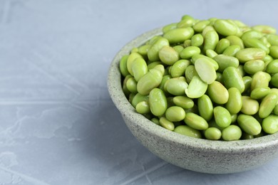 Photo of Fresh edamame soybeans in bowl on grey textured table, closeup. Space for text