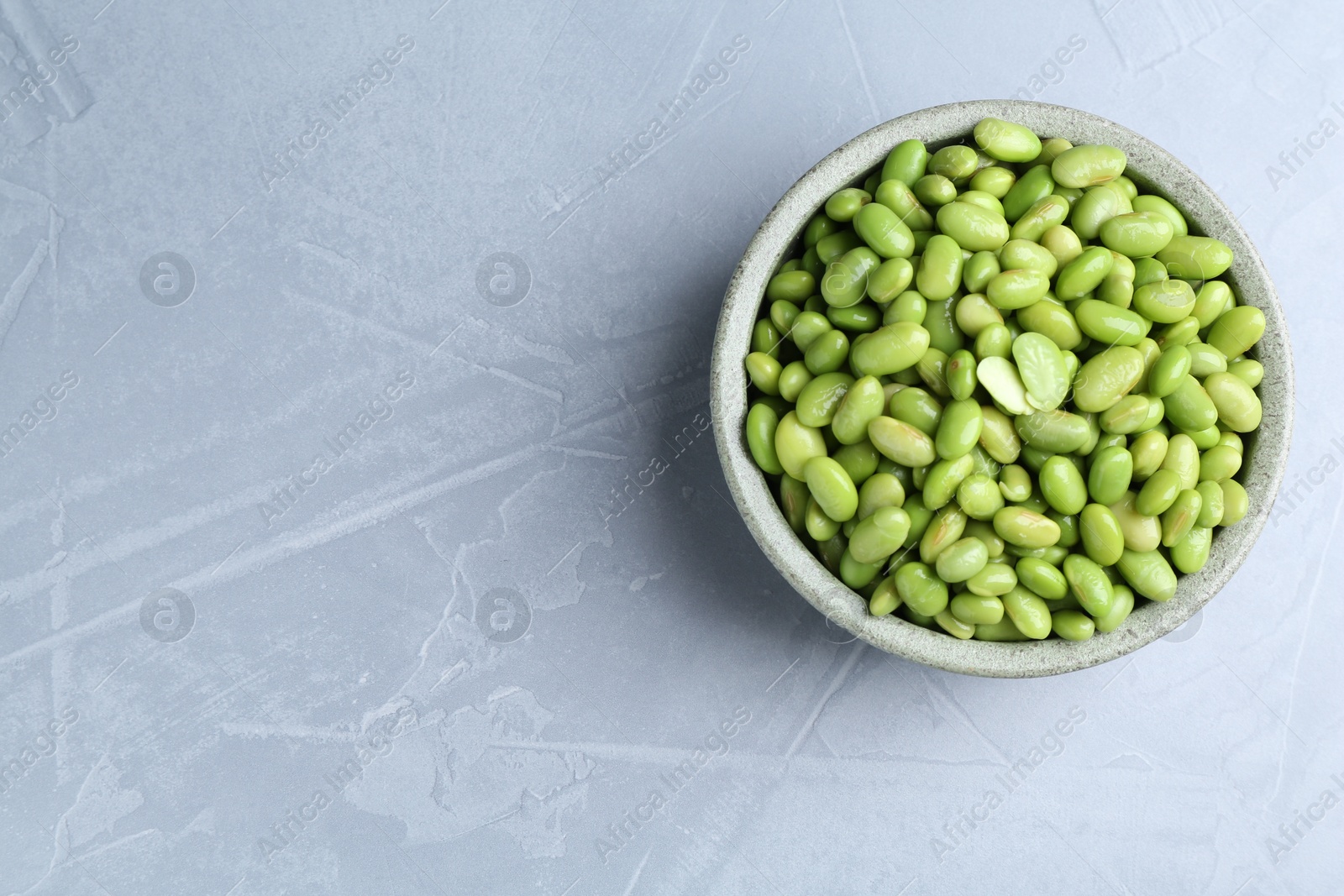 Photo of Fresh edamame soybeans in bowl on grey textured table, top view. Space for text