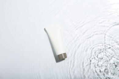 Photo of Cosmetic product. Tube with cream in water on light background, top view