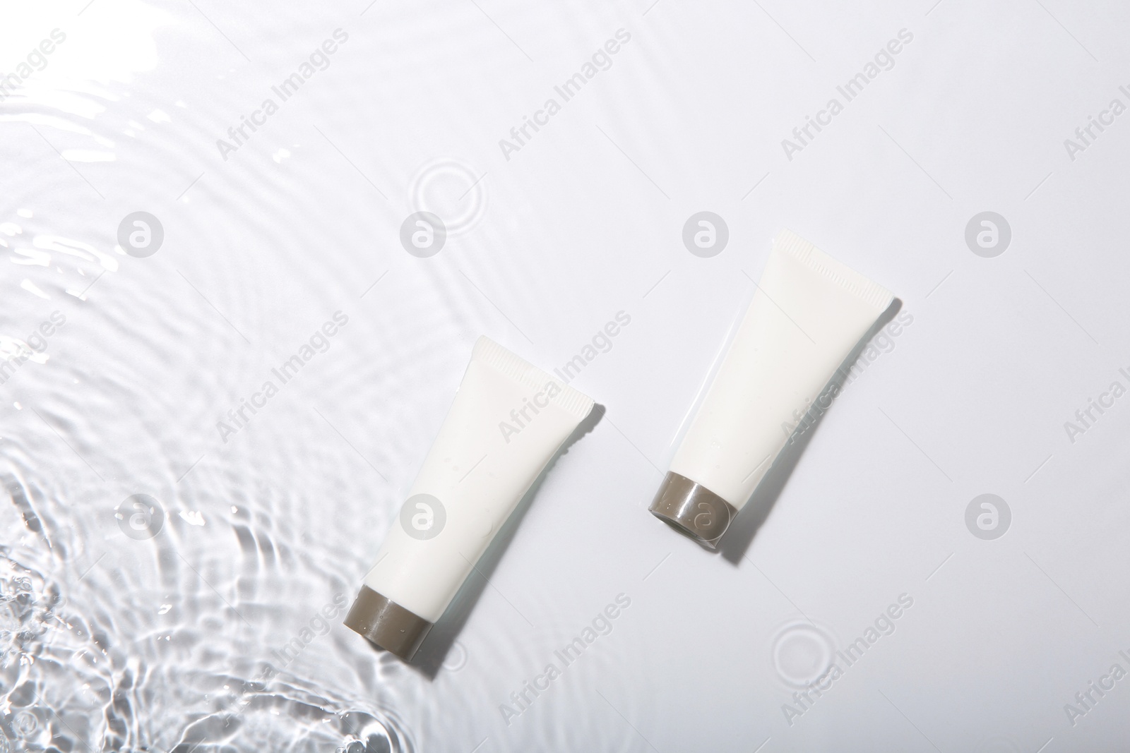 Photo of Cosmetic products. Tubes with cream in water on light background, top view