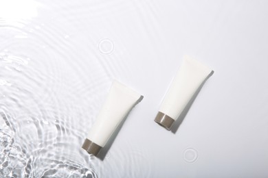 Photo of Cosmetic products. Tubes with cream in water on light background, top view