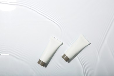 Cosmetic products. Tubes with cream in water on light background, top view