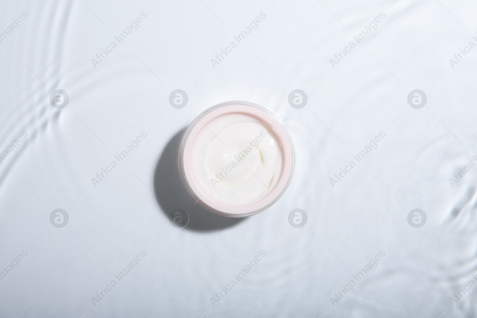 Photo of Cosmetic product. Jar with cream in water on light background, top view