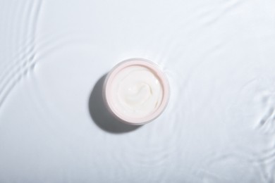 Cosmetic product. Jar with cream in water on light background, top view