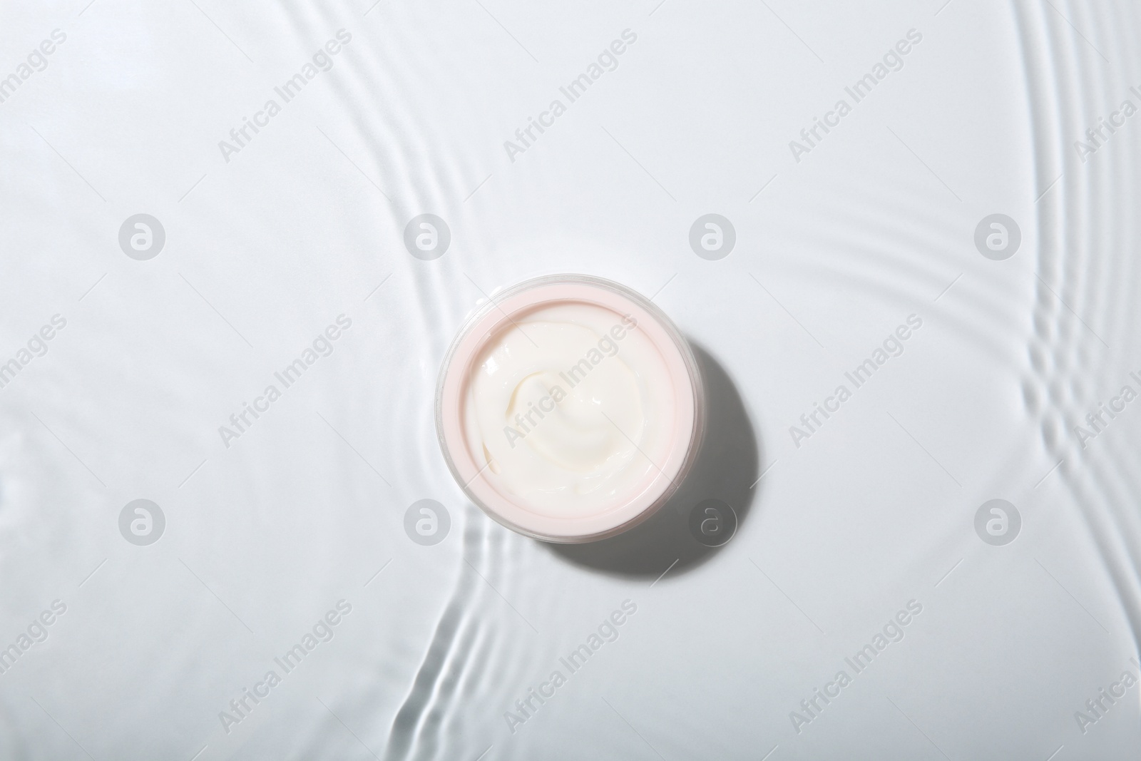 Photo of Cosmetic product. Jar with cream in water on light background, top view