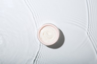 Photo of Cosmetic product. Jar with cream in water on light background, top view