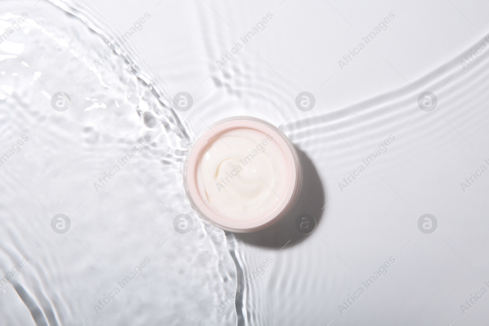 Photo of Cosmetic product. Jar with cream in water on light background, top view