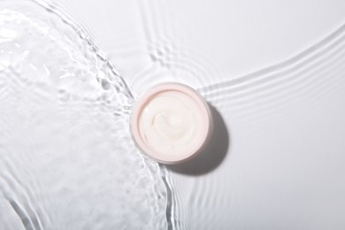 Photo of Cosmetic product. Jar with cream in water on light background, top view