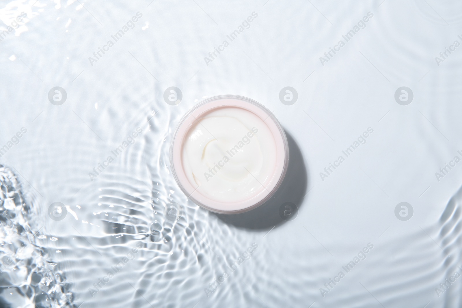 Photo of Cosmetic product. Jar with cream in water on light background, top view