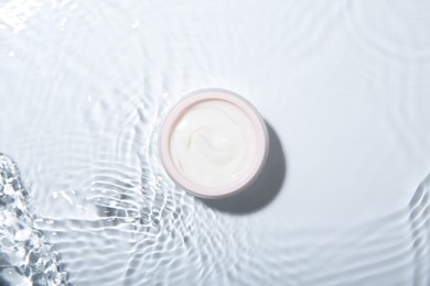 Cosmetic product. Jar with cream in water on light background, top view