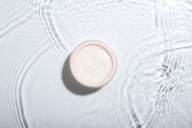 Photo of Cosmetic product. Jar with cream in water on light background, top view