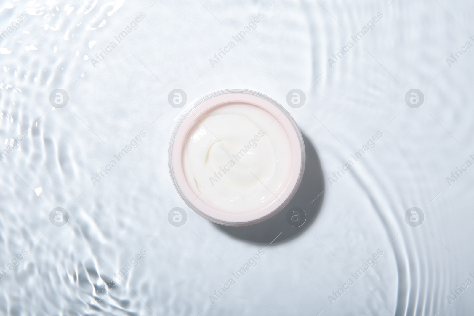 Photo of Cosmetic product. Jar with cream in water on light background, top view