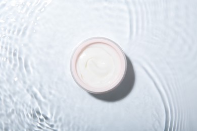 Cosmetic product. Jar with cream in water on light background, top view