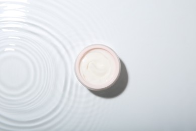 Photo of Cosmetic product. Jar with cream in water on light background, top view
