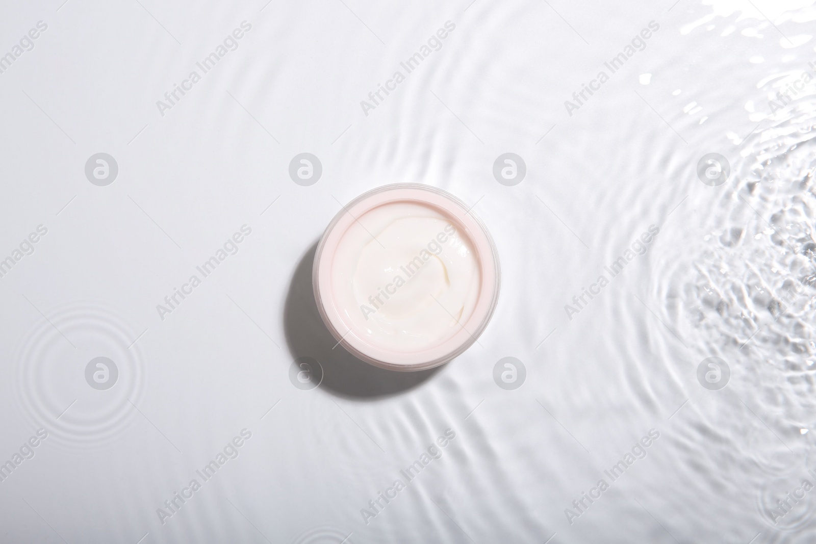 Photo of Cosmetic product. Jar with cream in water on light background, top view