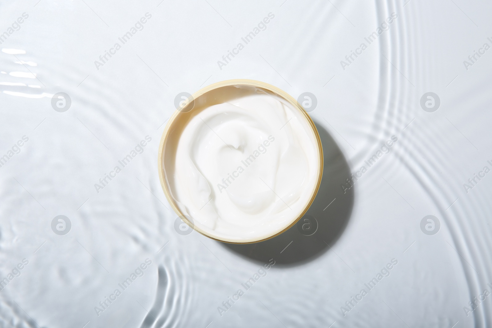 Photo of Cosmetic product. Jar with cream in water on light background, top view