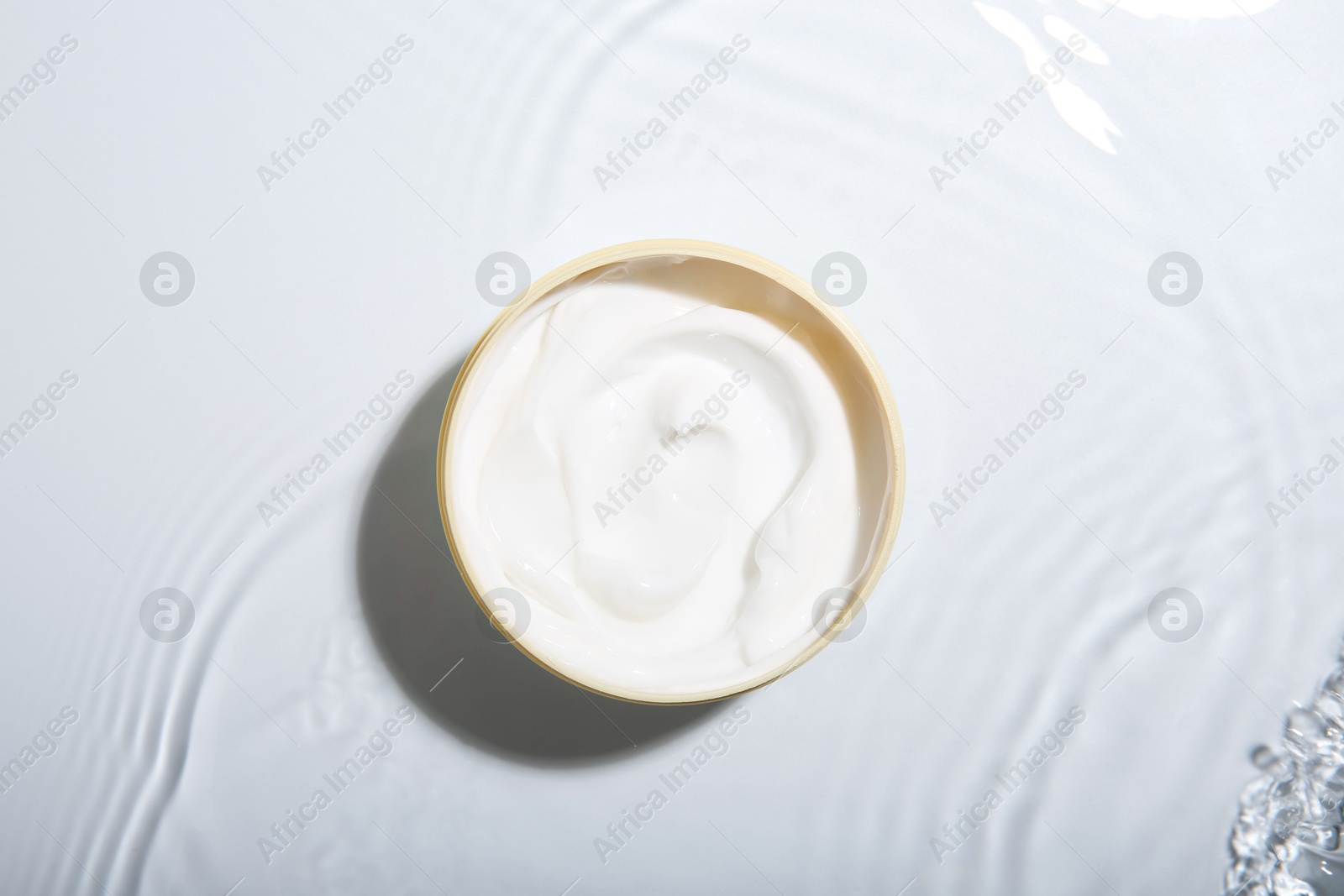 Photo of Cosmetic product. Jar with cream in water on light background, top view