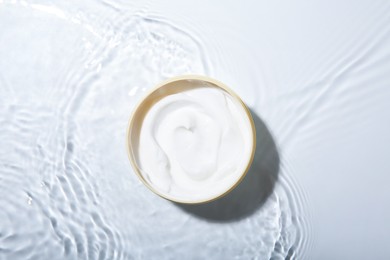 Photo of Cosmetic product. Jar with cream in water on light background, top view