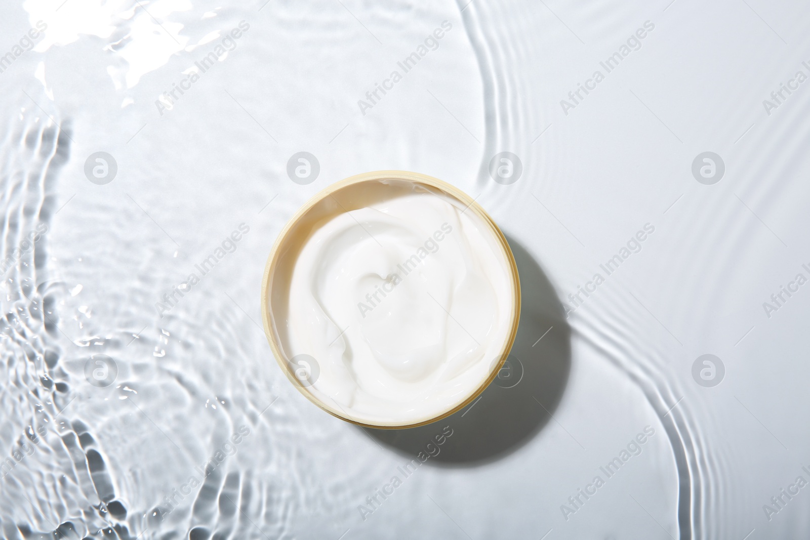 Photo of Cosmetic product. Jar with cream in water on light background, top view