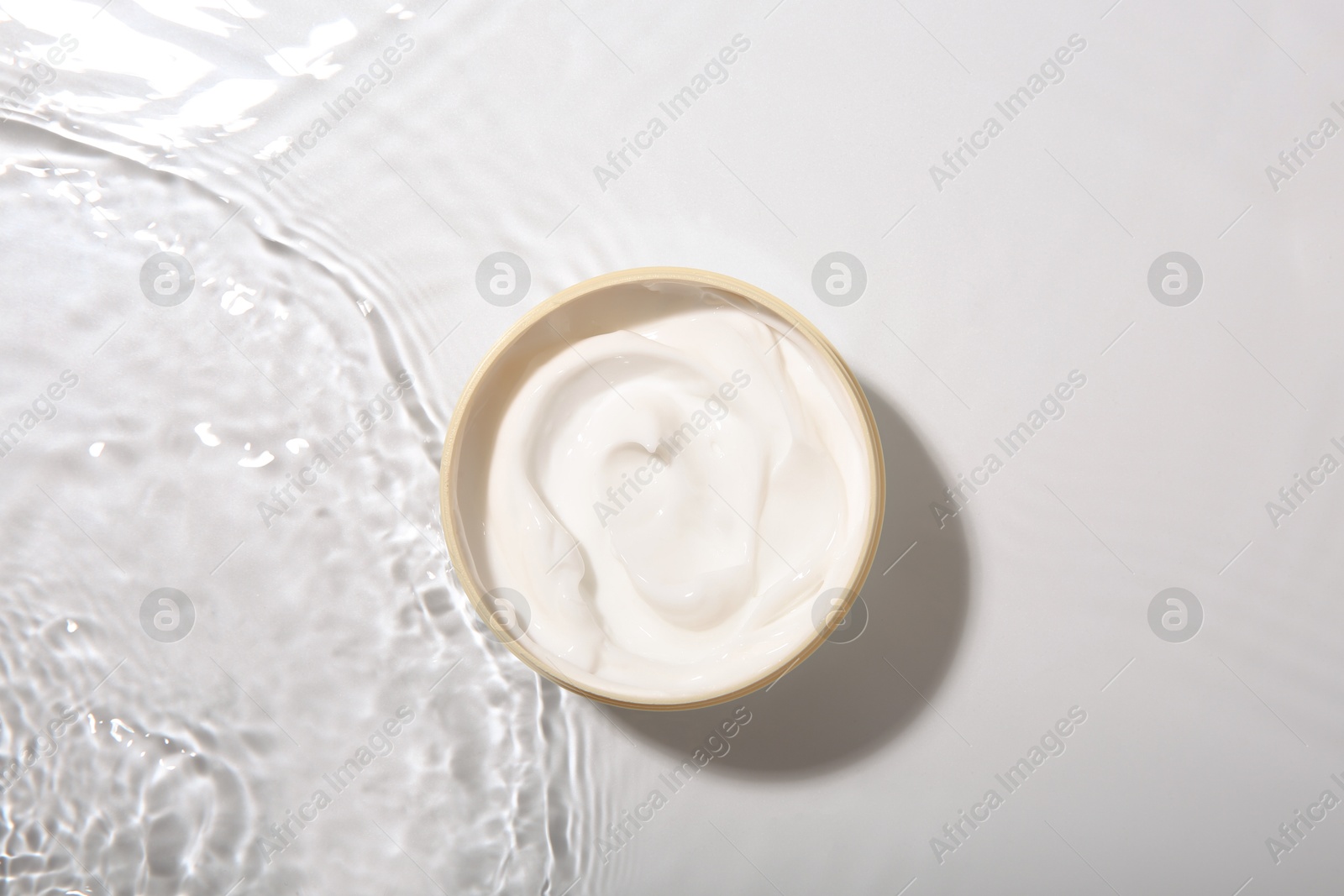 Photo of Cosmetic product. Jar with cream in water on light background, top view