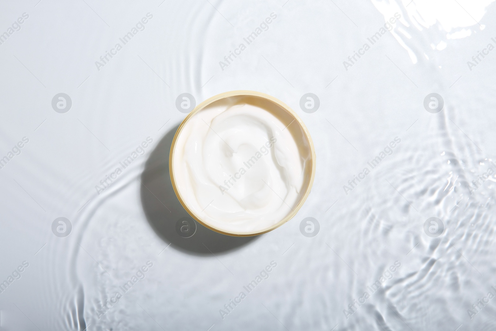 Photo of Cosmetic product. Jar with cream in water on light background, top view