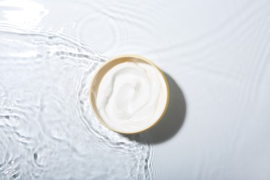 Photo of Cosmetic product. Jar with cream in water on light background, top view