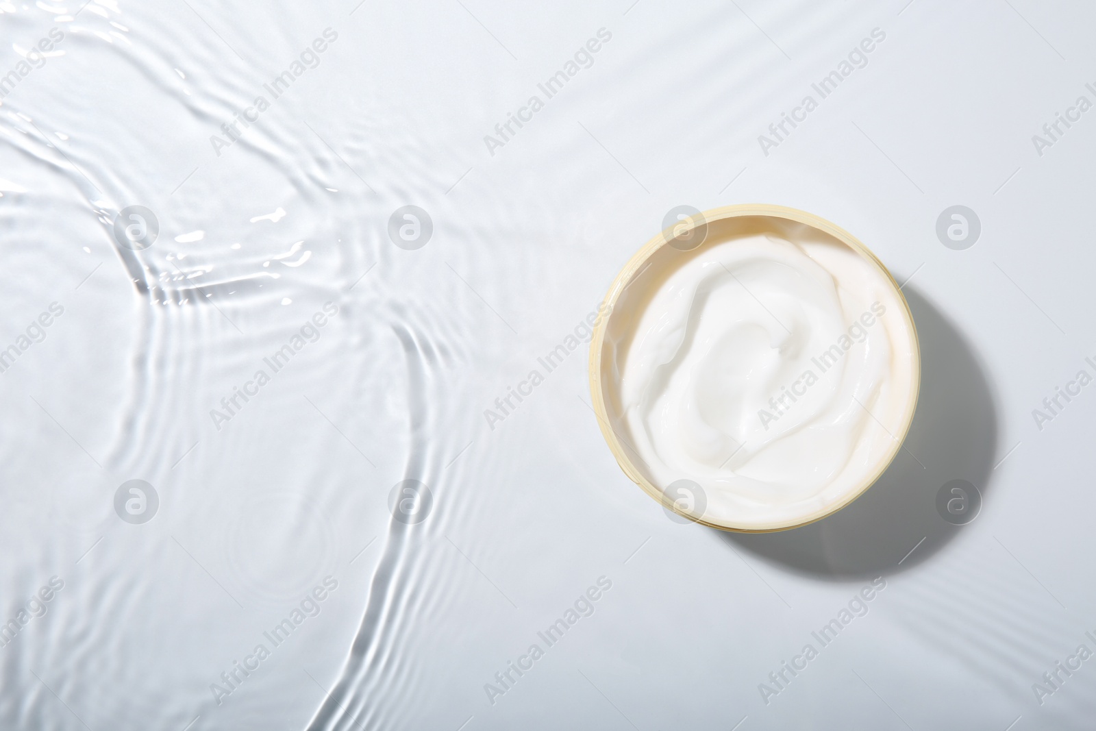 Photo of Cosmetic product. Jar with cream in water on light background, top view. Space for text