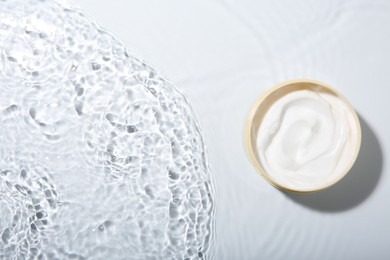 Photo of Cosmetic product. Jar with cream in water on light background, top view. Space for text