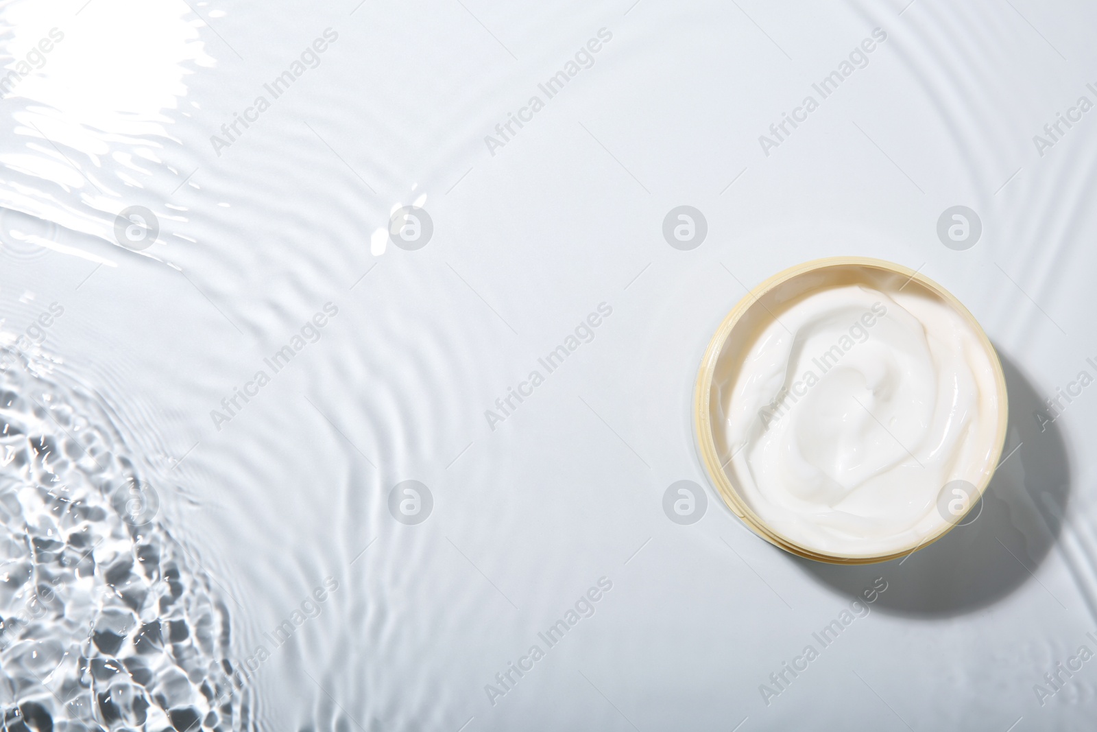 Photo of Cosmetic product. Jar with cream in water on light background, top view. Space for text