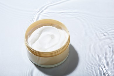 Photo of Cosmetic product. Jar with cream in water on light background