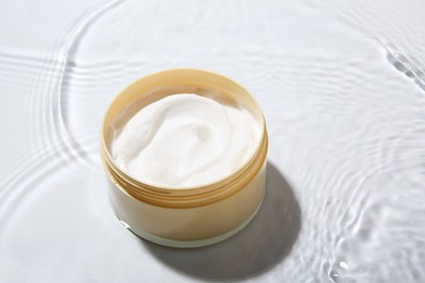 Photo of Cosmetic product. Jar with cream in water on light background