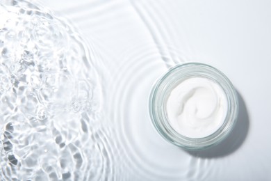 Photo of Cosmetic product. Jar with cream in water on light background, top view. Space for text