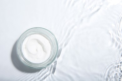 Photo of Cosmetic product. Jar with cream in water on light background, top view. Space for text
