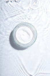 Photo of Cosmetic product. Jar with cream in water on light background, top view
