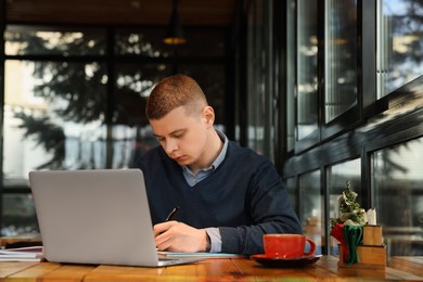 Photo of Young male student with laptop studying at table in cafe