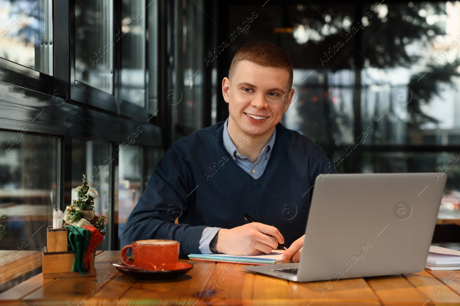 Photo of Young male student with laptop studying at table in cafe