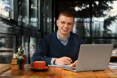 Young male student with laptop studying at table in cafe