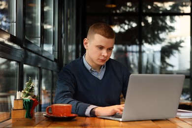 Photo of Young male student with laptop studying at table in cafe