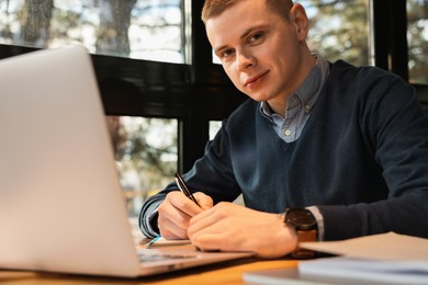 Photo of Young male student with laptop studying at table in cafe