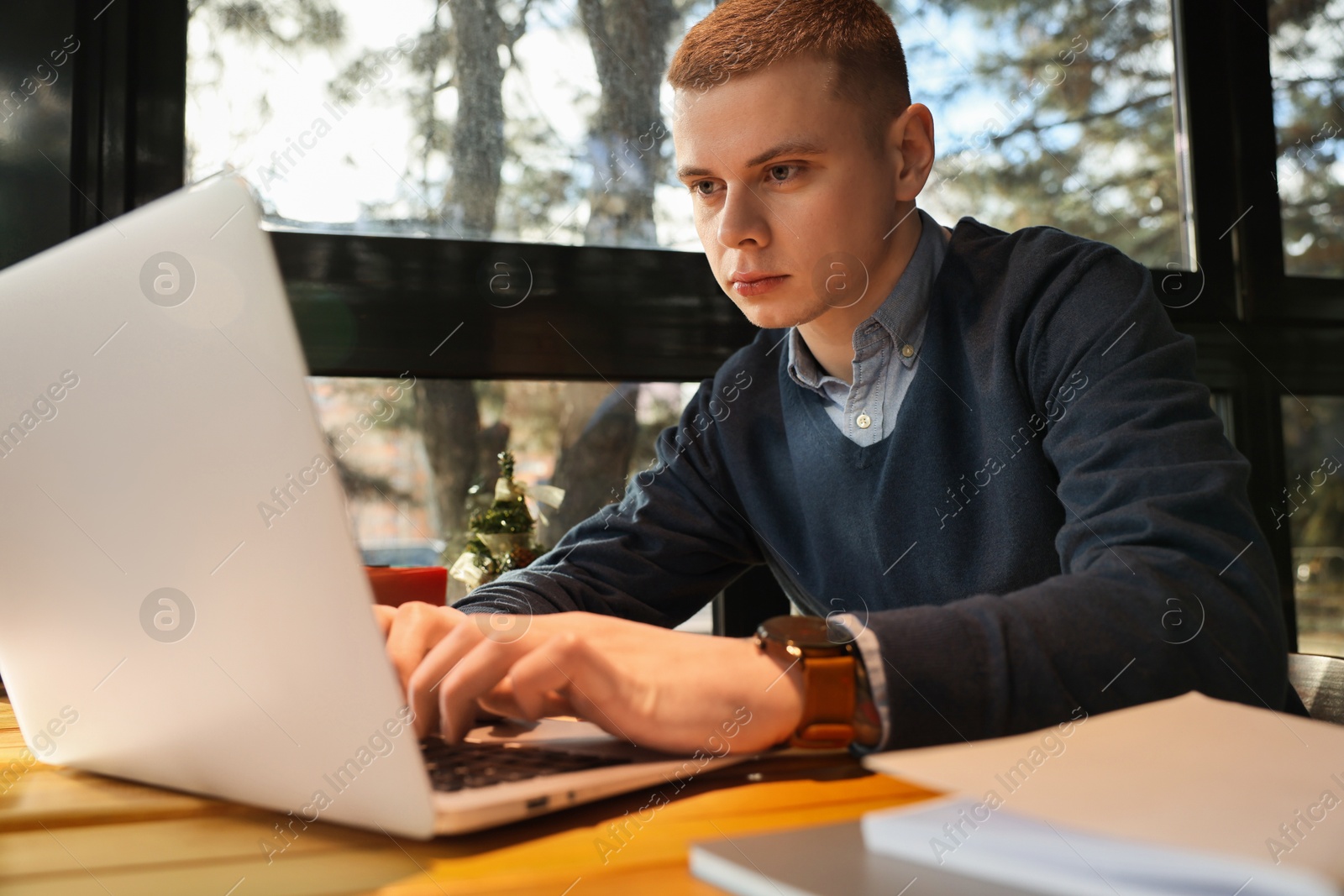 Photo of Young male student with laptop studying at table in cafe