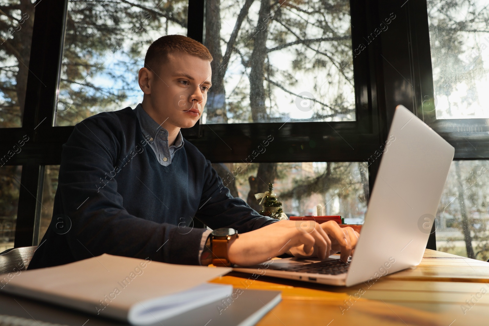 Photo of Young male student with laptop studying at table in cafe