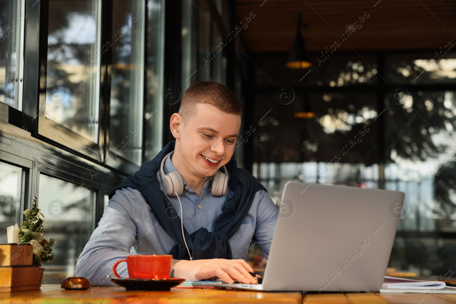 Photo of Young male student with laptop studying at table in cafe